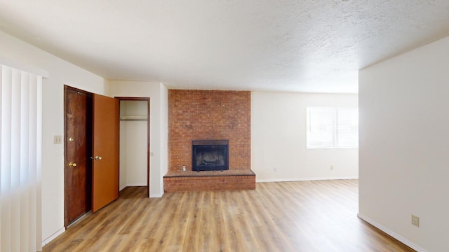 unfurnished living room with a brick fireplace, a textured ceiling, and light wood-type flooring