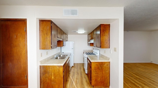 kitchen with light wood-type flooring, white appliances, a textured ceiling, and sink