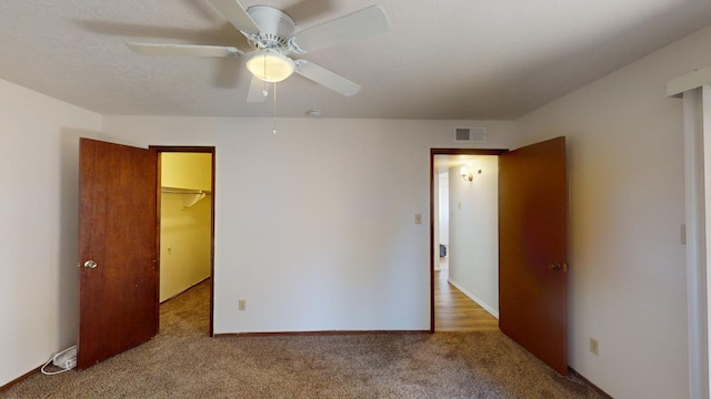 unfurnished bedroom with light carpet, ceiling fan, and a walk in closet