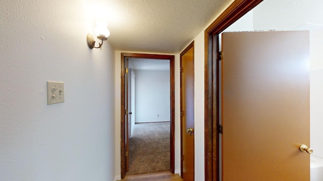 corridor featuring a textured ceiling and carpet flooring