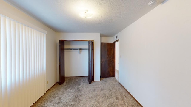 unfurnished bedroom featuring a textured ceiling, light colored carpet, and a closet