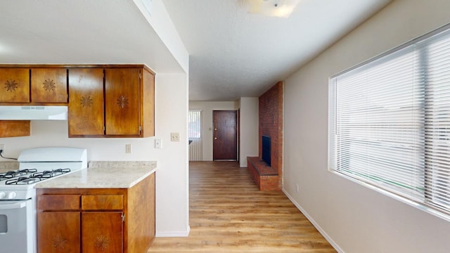 kitchen featuring a brick fireplace, light hardwood / wood-style flooring, gas range gas stove, and extractor fan