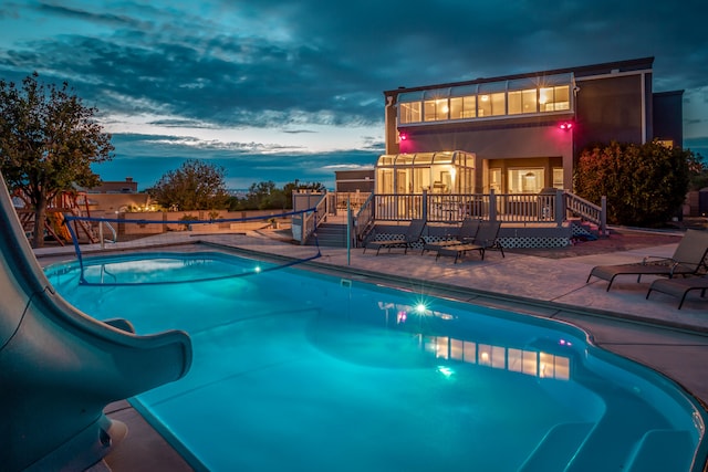 pool at dusk featuring a patio and a water slide