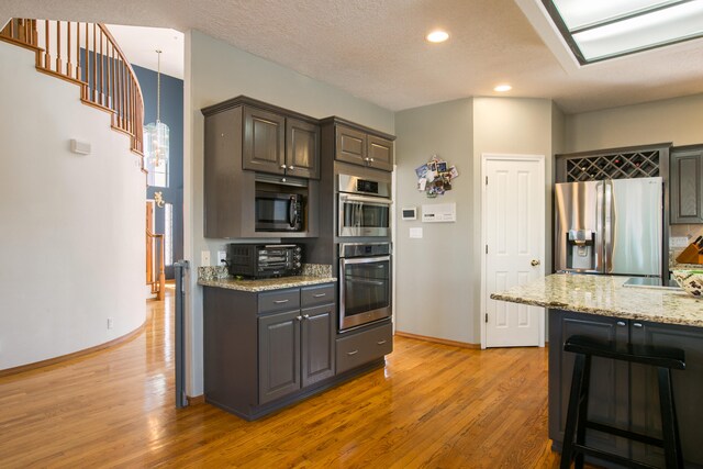 kitchen featuring light stone counters, pendant lighting, stainless steel appliances, light wood-type flooring, and a textured ceiling