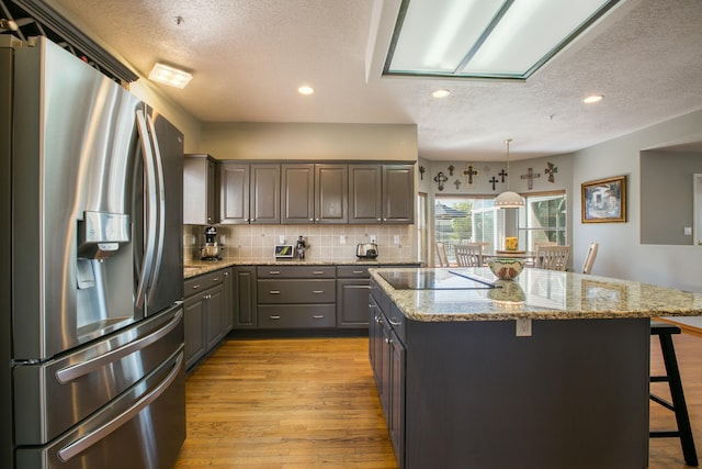 kitchen featuring stainless steel fridge, a kitchen island, light wood-type flooring, a kitchen bar, and decorative light fixtures