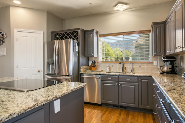 kitchen featuring light stone counters, sink, tasteful backsplash, appliances with stainless steel finishes, and light hardwood / wood-style floors