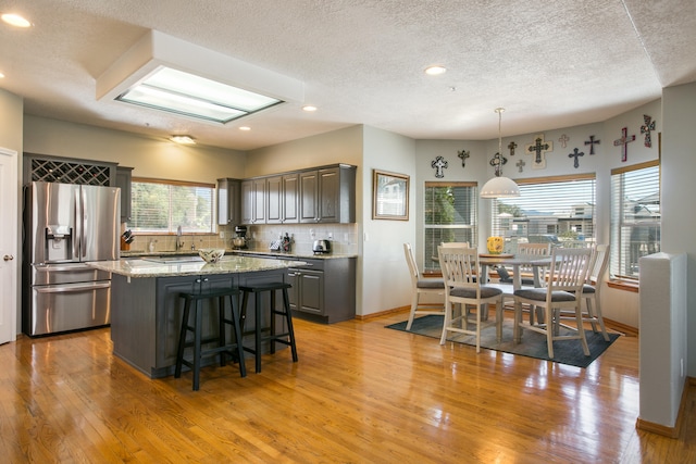 kitchen featuring stainless steel refrigerator with ice dispenser, light hardwood / wood-style floors, a textured ceiling, and a kitchen island