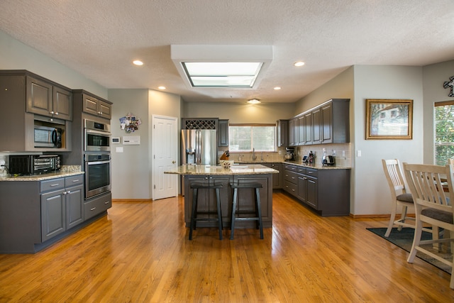 kitchen with appliances with stainless steel finishes, a center island, light hardwood / wood-style flooring, and light stone counters