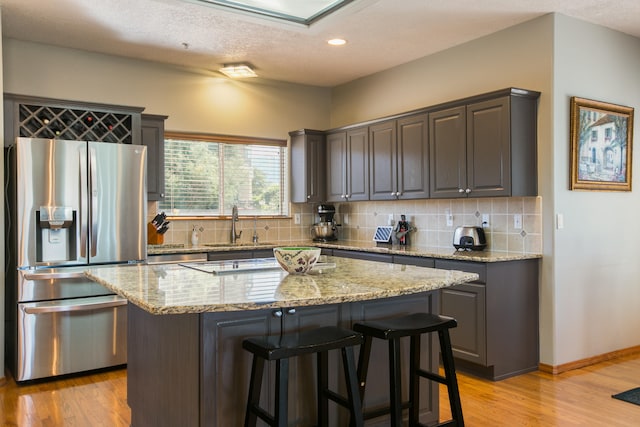 kitchen featuring a kitchen island, light stone countertops, a textured ceiling, light hardwood / wood-style flooring, and stainless steel fridge with ice dispenser