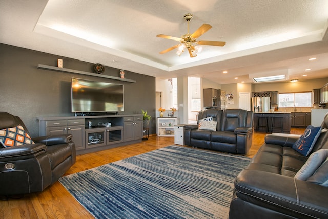 living room with ceiling fan, a raised ceiling, sink, a textured ceiling, and hardwood / wood-style flooring