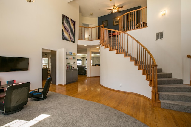 living room featuring a towering ceiling, ceiling fan, and hardwood / wood-style flooring