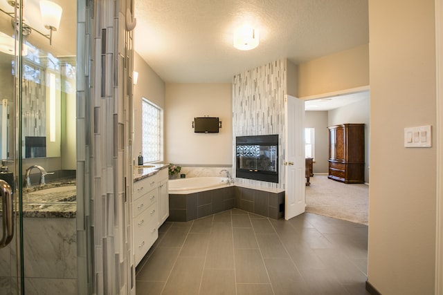 bathroom featuring vanity, a multi sided fireplace, tiled tub, a textured ceiling, and tile patterned flooring