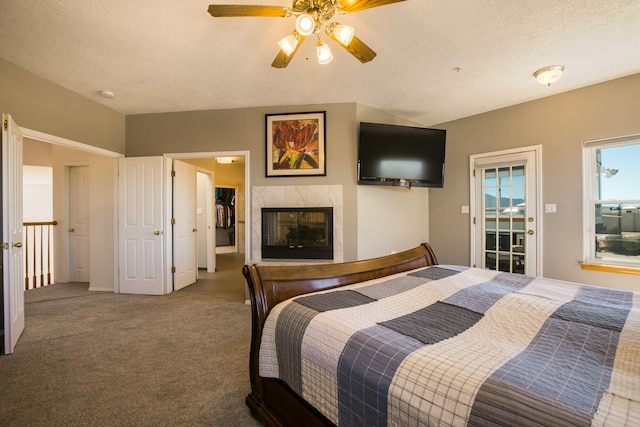 carpeted bedroom featuring a tiled fireplace, a textured ceiling, and ceiling fan