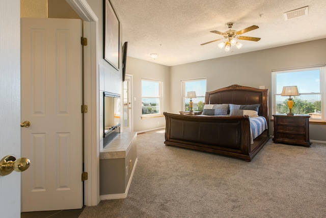 bedroom featuring ceiling fan, light colored carpet, a textured ceiling, and a fireplace