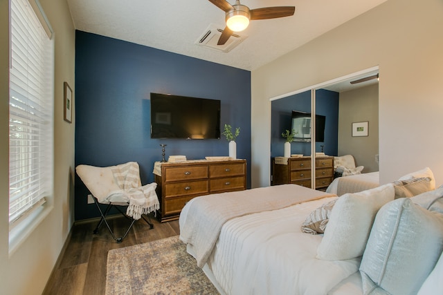 bedroom featuring multiple windows, dark hardwood / wood-style floors, ceiling fan, and a closet