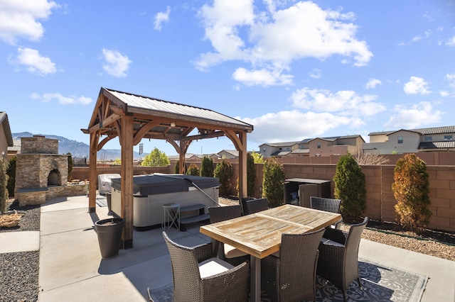 view of patio with outdoor dining area, an outdoor stone fireplace, a hot tub, a gazebo, and a fenced backyard