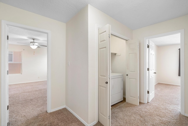 hallway featuring a textured ceiling, washer / dryer, and light colored carpet