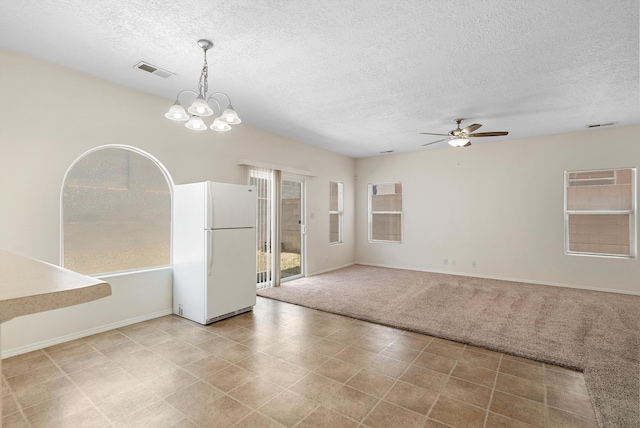 carpeted empty room featuring a textured ceiling and ceiling fan with notable chandelier