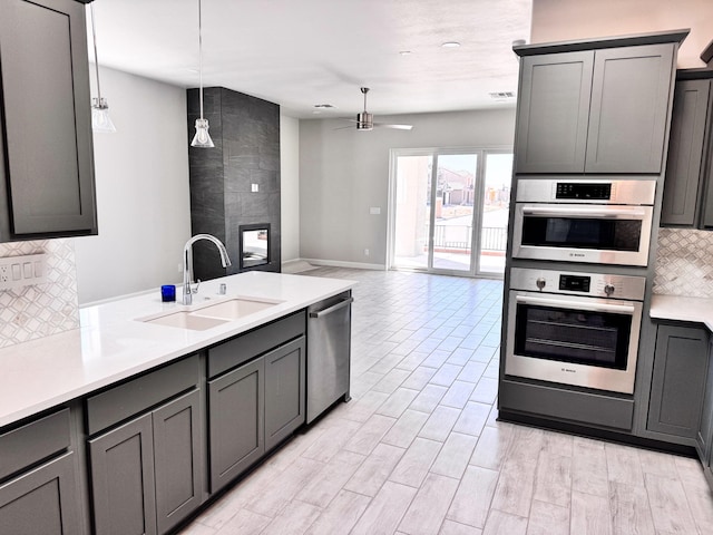 kitchen with hanging light fixtures, a fireplace, gray cabinets, ceiling fan, and sink