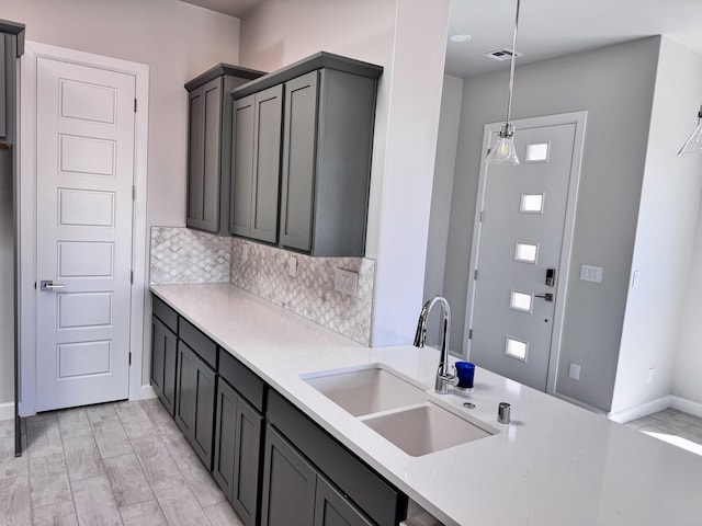 kitchen with pendant lighting, light wood-type flooring, tasteful backsplash, sink, and light stone countertops