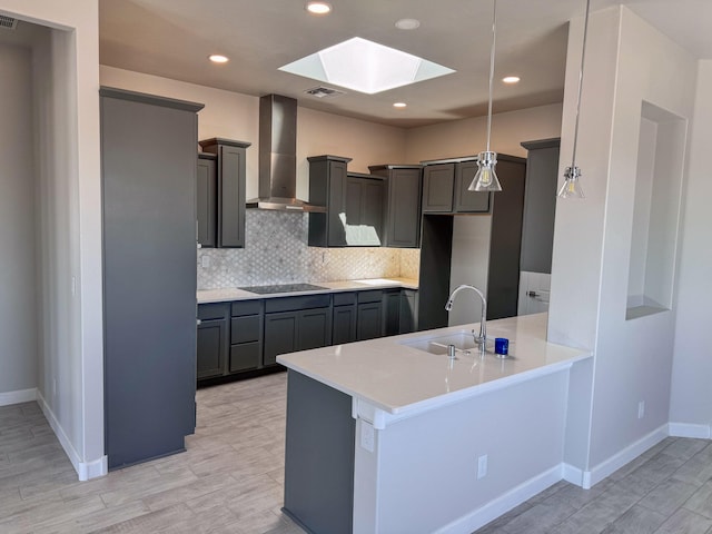 kitchen with a skylight, hanging light fixtures, kitchen peninsula, sink, and wall chimney exhaust hood