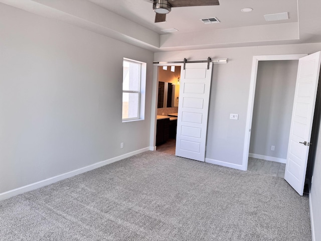 unfurnished bedroom featuring a barn door, ensuite bath, ceiling fan, and carpet floors