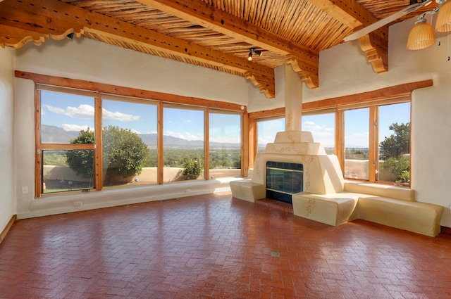 unfurnished living room featuring beam ceiling, wood ceiling, a mountain view, and ceiling fan