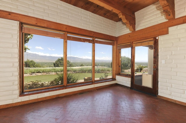 unfurnished sunroom with brick floor, a mountain view, wooden ceiling, and beam ceiling