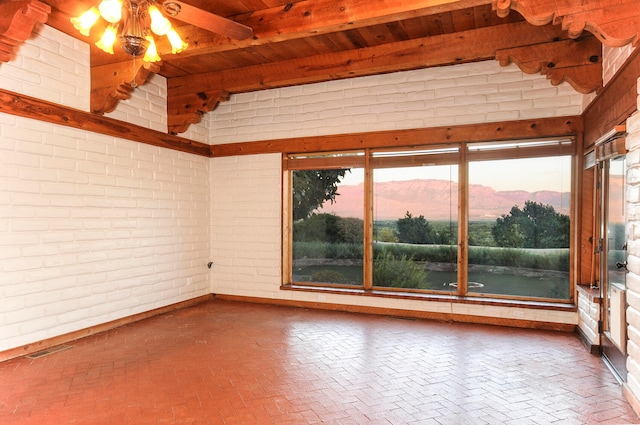 spare room with brick wall, a mountain view, beam ceiling, and ceiling fan