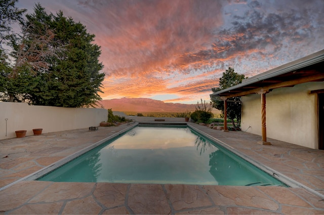 pool at dusk featuring a mountain view and a patio area