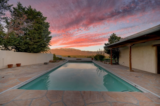 pool at dusk featuring a mountain view and a patio area