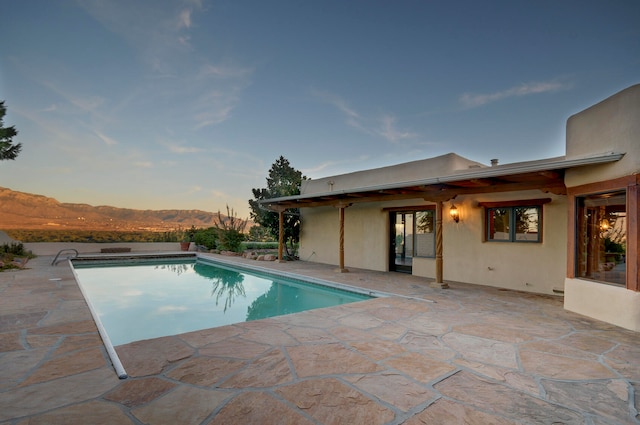 pool at dusk featuring a mountain view and a patio