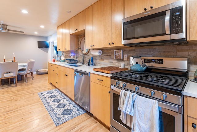 kitchen with ceiling fan, sink, tasteful backsplash, appliances with stainless steel finishes, and light hardwood / wood-style floors