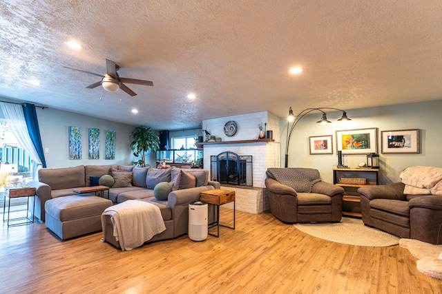 living room with light hardwood / wood-style flooring, ceiling fan, a textured ceiling, and a fireplace