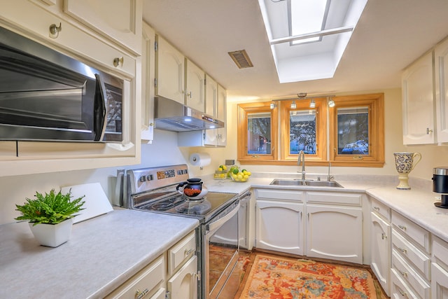 kitchen with appliances with stainless steel finishes, white cabinetry, sink, and a skylight