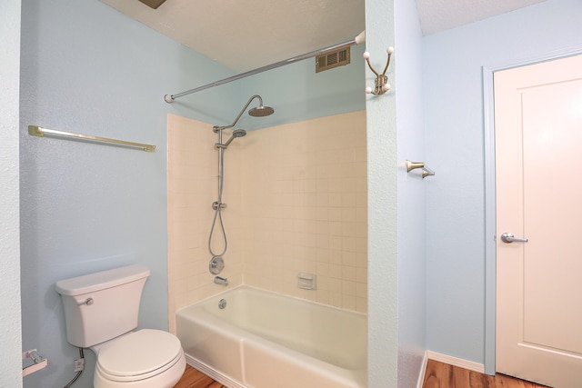 bathroom with tiled shower / bath combo, a textured ceiling, hardwood / wood-style flooring, and toilet