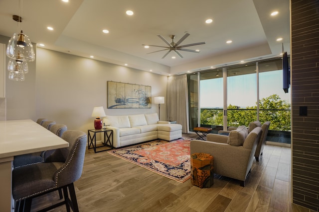 living room with a tray ceiling, ceiling fan, hardwood / wood-style floors, and expansive windows