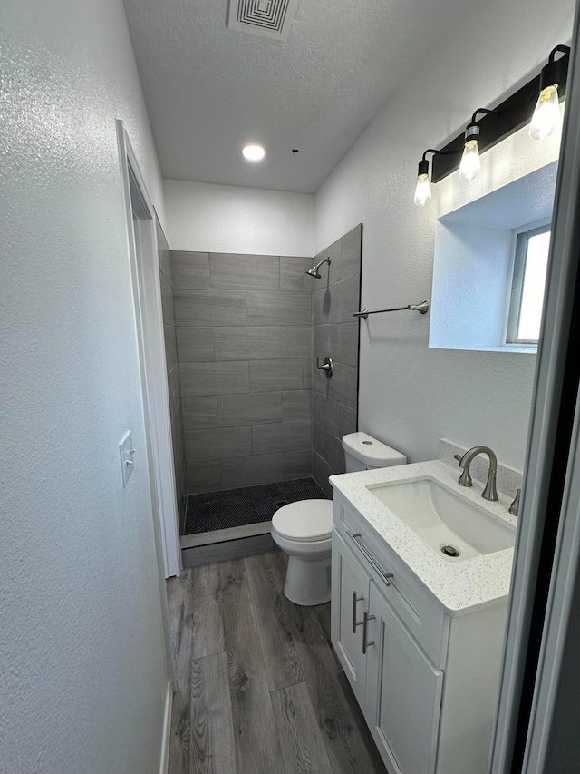 bathroom with tiled shower, vanity, toilet, and hardwood / wood-style flooring