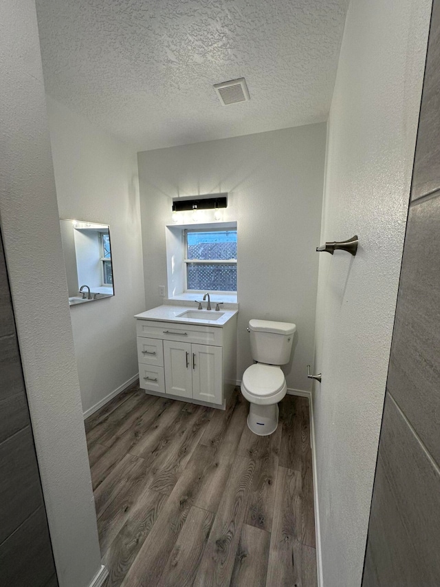 bathroom with a textured ceiling, hardwood / wood-style flooring, vanity, and toilet