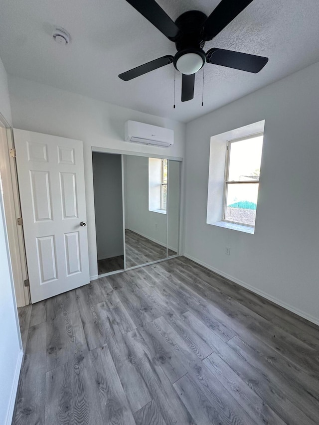 unfurnished bedroom with an AC wall unit, a closet, ceiling fan, and hardwood / wood-style floors