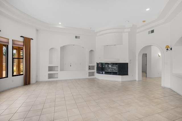 unfurnished living room with built in shelves, a towering ceiling, and light tile patterned floors