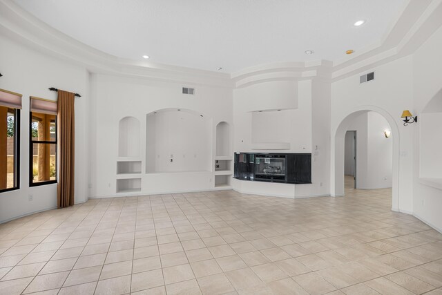 1220 Mesa Ridge Dr SW, Los Lunas, NM 87031 - unfurnished living room with a towering ceiling, a tray ceiling, built in shelves, recessed lighting, and light tile patterned floors