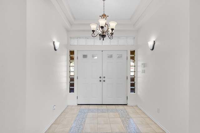 tiled entryway featuring ornamental molding, a tray ceiling, and a chandelier