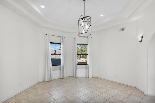 tiled spare room with an inviting chandelier and a raised ceiling