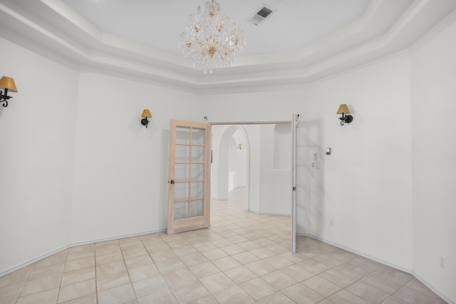 tiled spare room with french doors, a tray ceiling, and a chandelier