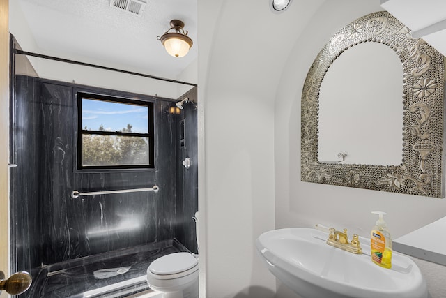 bathroom with a tile shower, sink, and toilet