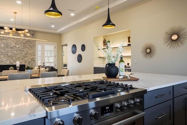 kitchen featuring light stone countertops, stainless steel stove, and hanging light fixtures