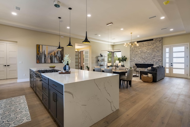 kitchen with hanging light fixtures, light hardwood / wood-style floors, a stone fireplace, a kitchen island, and light stone countertops