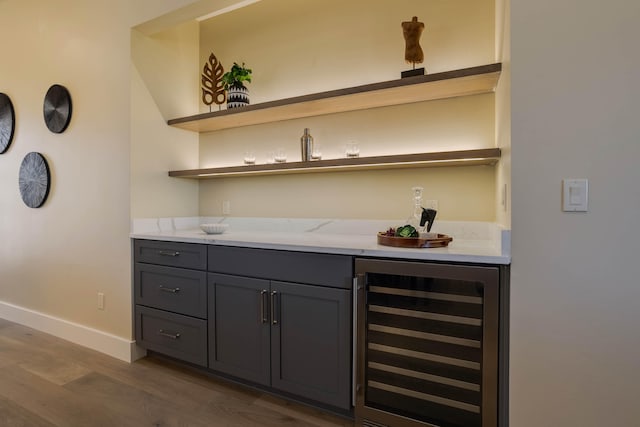 bar with gray cabinetry, wine cooler, light stone counters, and dark hardwood / wood-style flooring