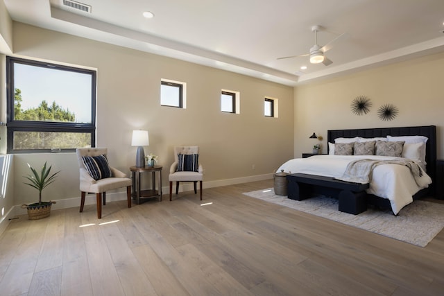 bedroom with light wood-type flooring, a tray ceiling, and ceiling fan